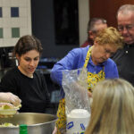 A group of parishioners in gloves and aprons, preparing food for a charitable dinner