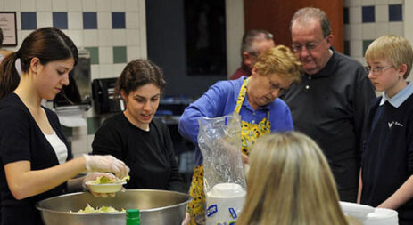 A group of parishioners in gloves and aprons, preparing food for a charitable dinner
